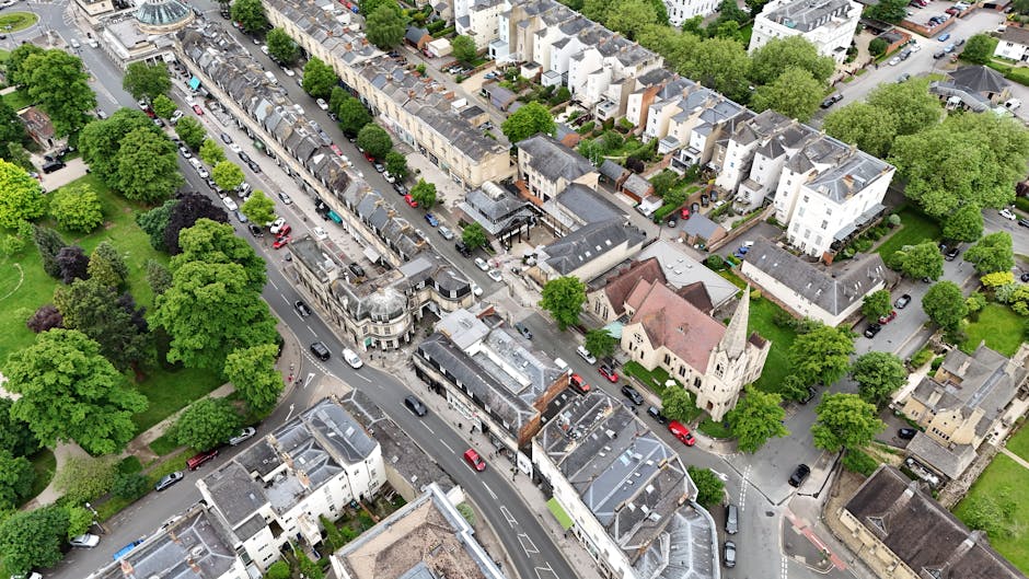 An aerial view of North Finchley High Road showing a busy street with lined parked cars on both sides, surrounded by rows of residential buildings and small commercial properties. The pavement is popu