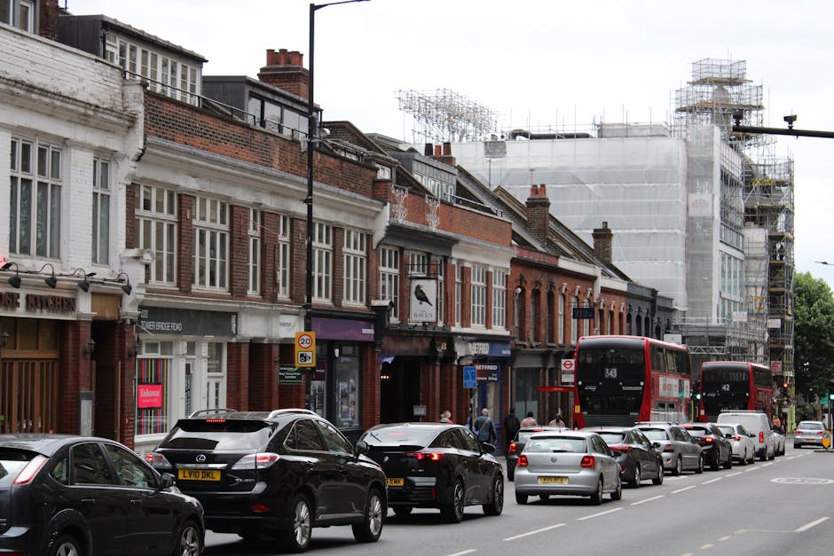 An aerial view of North Finchley High Road showing a busy street with lined parked cars on both sides, surrounded by rows of residential buildings and small commercial properties. The pavement is popu